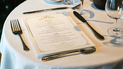 A menu lying on a table in a restauraunt framed by cutlery