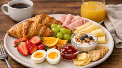A classic continental breakfast spread with fresh croissants, brioche, butter, jam, a steaming bowl of cafe au lait, and freshly squeezed orange juice on a linen-covered table