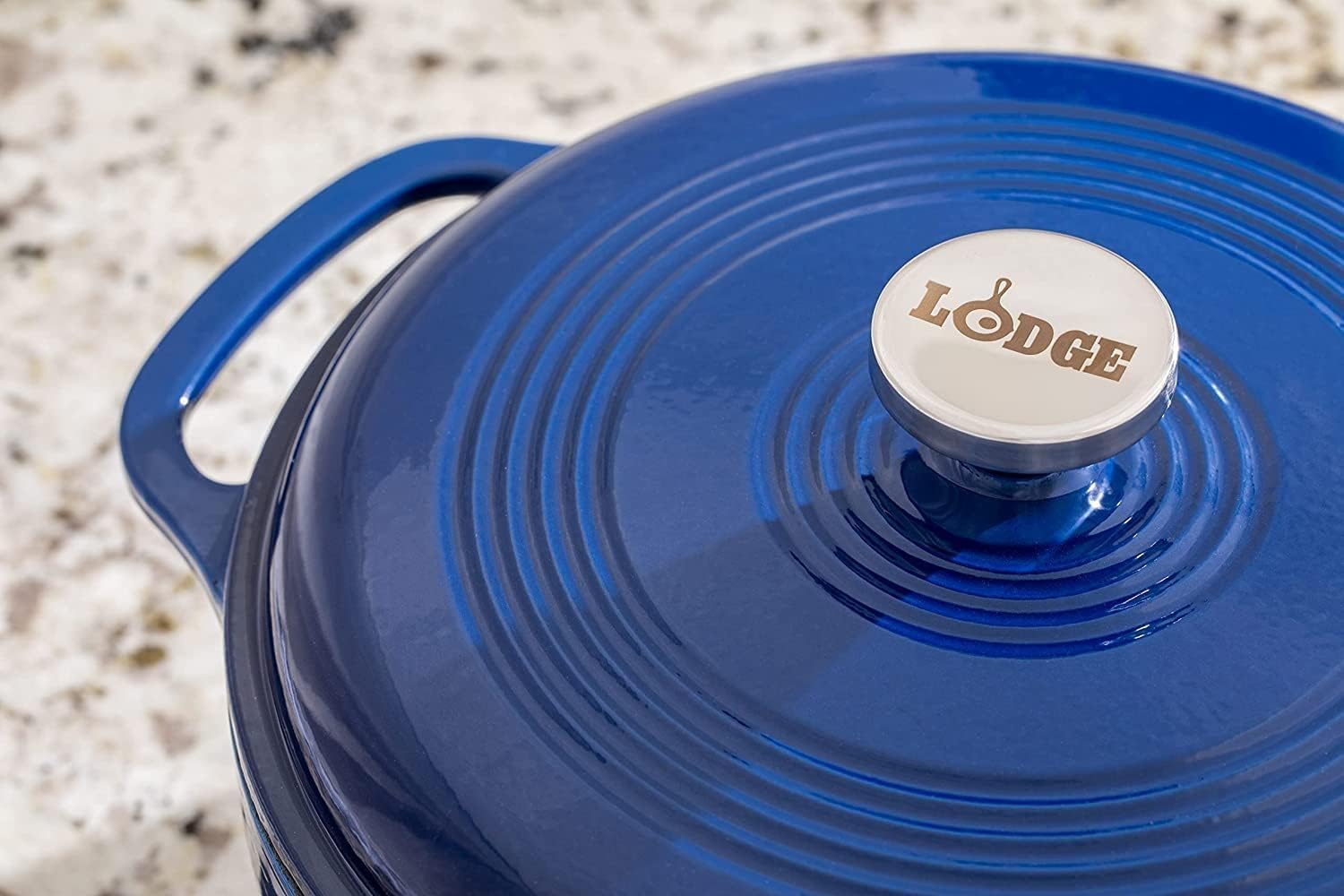 Lodge 7.5 Quart enameled cast iron Dutch oven in blue with stainless steel lid knob, sitting on a gas stove
