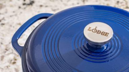Lodge 7.5 Quart enameled cast iron Dutch oven in blue with stainless steel lid knob, sitting on a gas stove