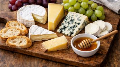 A traditional French cheese board featuring a selection of Brie, Camembert, Comté, Roquefort, and goat cheese, arranged on a wooden board with fresh baguette slices, grapes, and a small dish of honey.